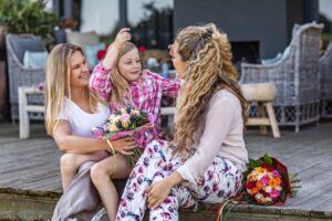 Famiglia omogenitoriale con figlia sorridente e mazzi di fiori, simbolo di affetto e riconoscimento legale del ruolo di entrambe le madri come genitori